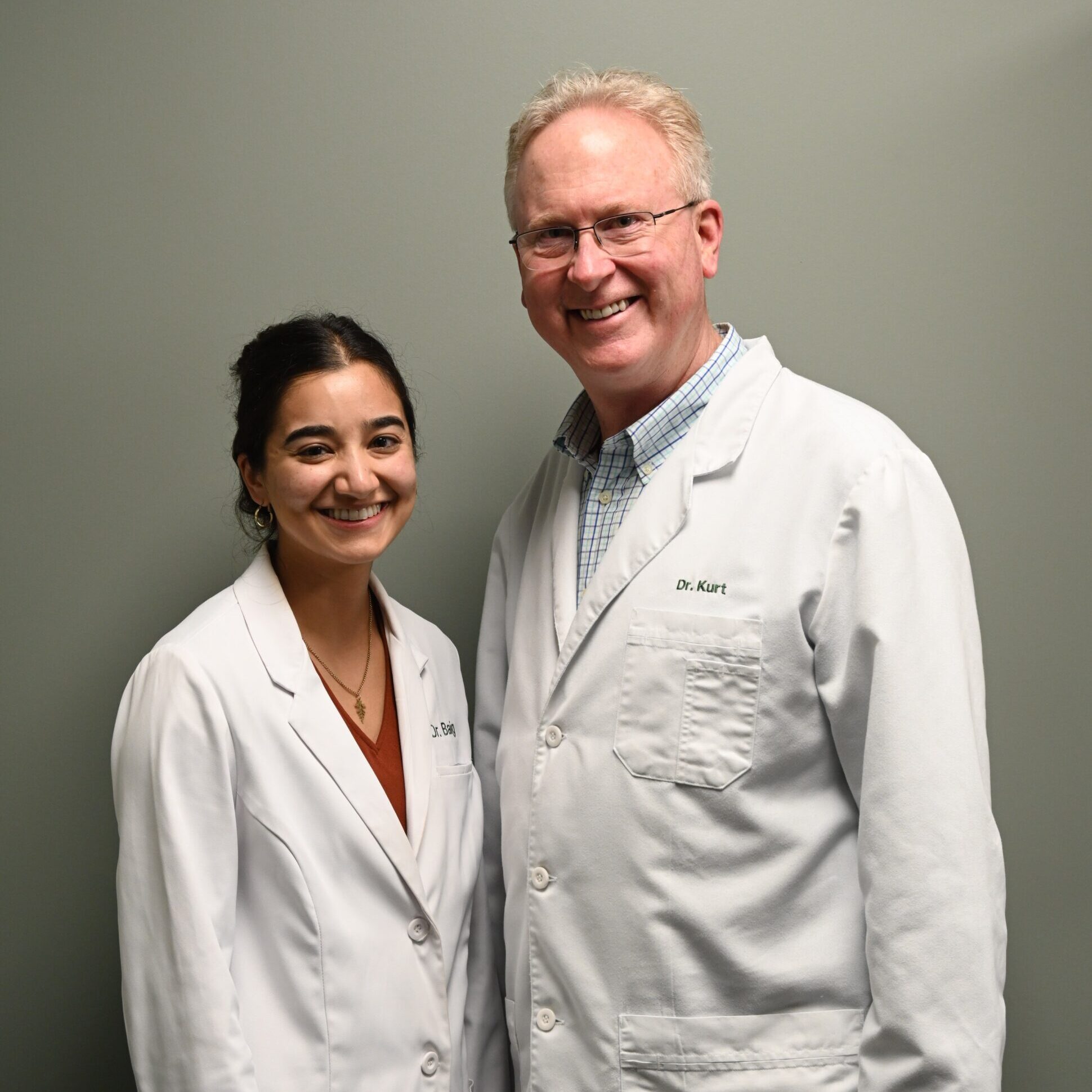 Dr. Kurt Kavanaugh and Dr. Emily, orthodontic professionals in white lab coats, smiling against a neutral background, representing a welcoming orthodontic team in Kansas City.